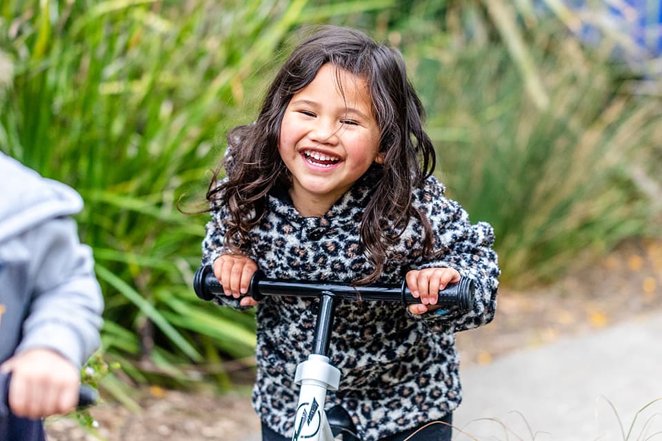 Young girl smiling at camera while riding a scooter in Glendene daycare