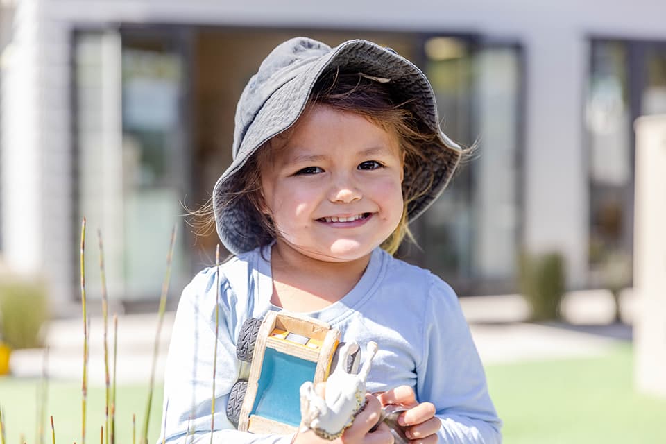Young girl in hat smiling at camera at Onehunga daycare