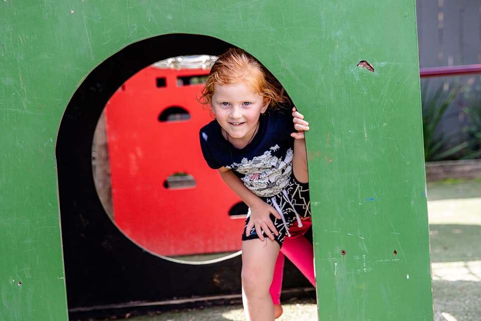 Young child hiding in playground looking at camera