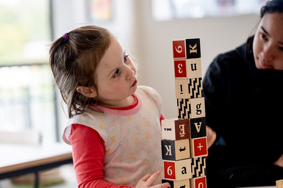 Girl intently stacking letter blocks at daycare in Glen Eden.