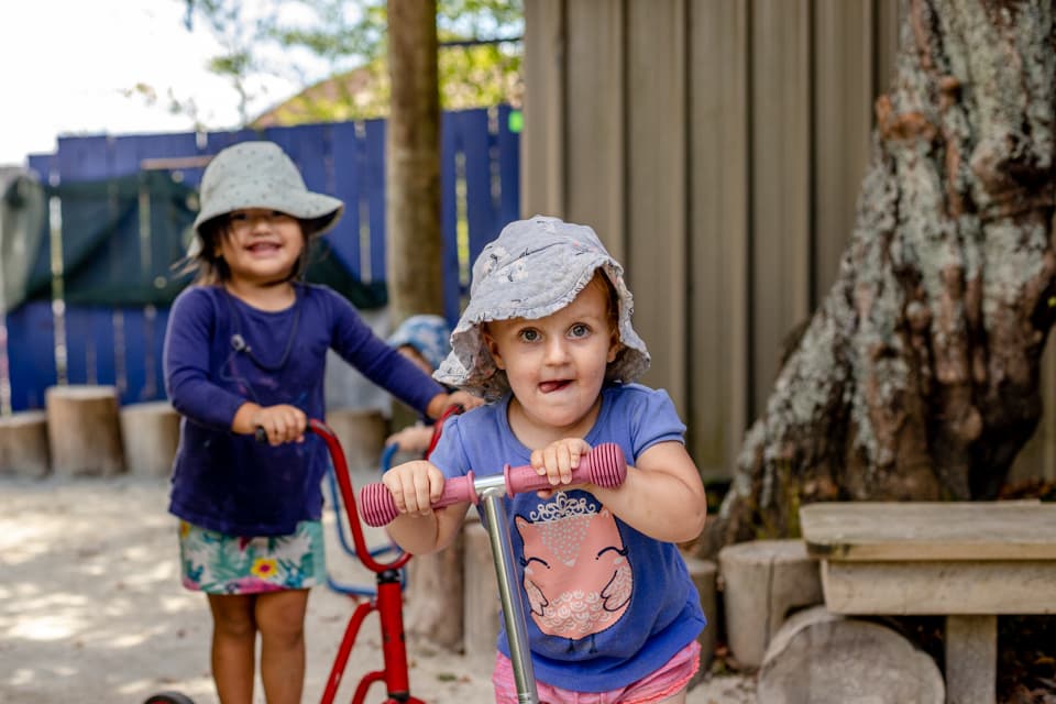 young girl on scooter looking at camera cheekily at daycare in glendene