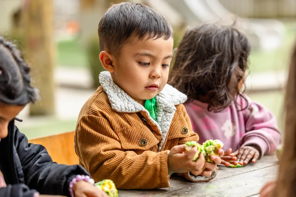 Young child focused on exploring playdough at an outdoor table with other children at Our Kids Early Learning Centre